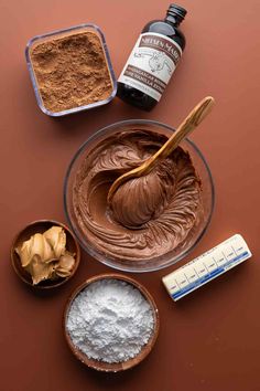 ingredients to make chocolate frosting in bowls on a brown surface with spoons and measuring tape