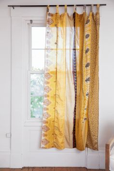 an open window with yellow and orange curtains hanging from it's sides, in front of a white wall