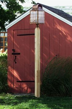 a red shed with a light on the side and grass in front, next to it