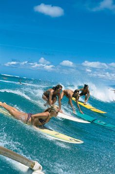 four surfers are riding the waves on their surfboards in the blue sky and white clouds