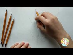 someone is drawing something with pencils on the paper and another hand next to it