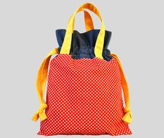 a red and white polka dot backpack with yellow straps on the front, sitting against a gray background