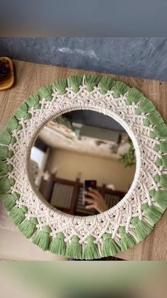 a green and white mirror sitting on top of a wooden table next to a vase