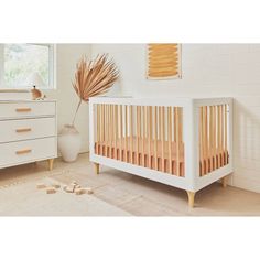 a baby crib in a white room next to a dresser with a potted plant