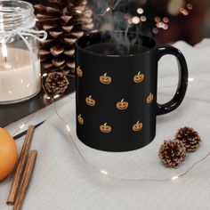 a black coffee mug with pumpkins on it next to cinnamon sticks and pine cones