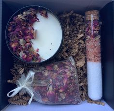 an open box containing two candles and some dried flowers next to a candle in a bag