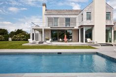 a woman standing in front of a house next to a swimming pool with lounge chairs