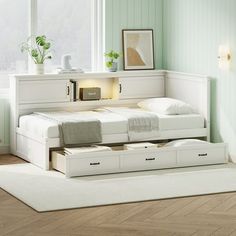 a white bed with two drawers underneath it in a room that has light green walls and hardwood floors