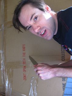 a man holding a knife in front of a cardboard box