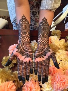 two hands with henna designs on them sitting next to flowers in front of a woman's face