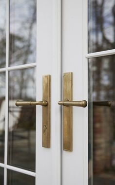 a close up of a door handle on a white door with glass panes and trees in the background