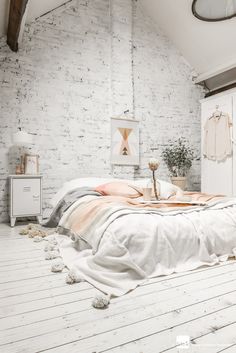 a bedroom with white brick walls and bedding in the corner, along with potted plants