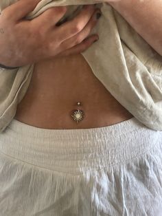 a woman wearing a white top with a sun charm on her chest and the bottom part of her stomach