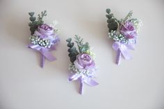 three small boutions with purple flowers and greenery are arranged on a white surface