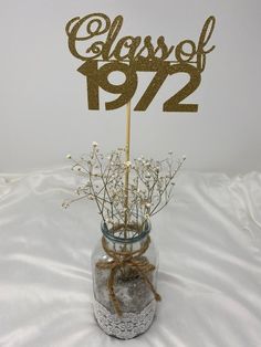 a glass vase filled with flowers and a cake topper that says class of 1971