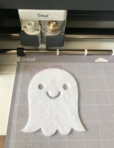 a cut out ghost on a cutting mat next to a machine with the word cricut printed on it