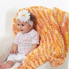 a baby sitting in a chair with a blanket on it's back and a flower in her hair