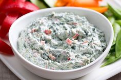 a white plate topped with a bowl of dip next to veggies and tomatoes