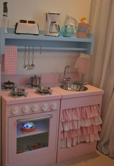 a pink play kitchen with blue shelves and white curtains