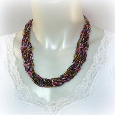 Desert Hues Ladder Yarn Necklace. Hand-crocheted from luxury trellis yarns, this model is done in soft shades of pink, purple, gray and gold. Lustrous and light as a feather, ladder yarn necklaces are perfect for any fashion style. Adjustable from approximately 14 to 30 inches (38-77 cm), just slip it over your head and slide the bead to make it matinee or opera length, a romantic choker or turned around as a chic lariat.  These simple necklaces make great gifts for long-time friends as well as casual associates of all ages. Wonderful for travel, they're deal for anyone with sensitivity to metals or people who don't want to bother with fiddly claps. Bead may vary from necklace to necklace, but will always be complementary & tasteful. These necklaces are also easy care. If they get a little Ladder Yarn Necklace, Ladder Yarn, Crochet Necklaces, Yarn Necklace, Fiber Jewelry, Ribbon Necklace, Long Dangle Earrings, Gold Ribbons, Lariat Necklace