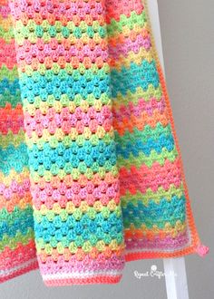 a multicolored crocheted blanket hanging on a clothes rack next to a wall