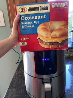 a person holding up a box of jimmy dean croissant and egg sandwich in front of an air fryer