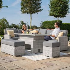 a man and woman sitting at an outdoor table with grey cushions on it in the middle of a patio