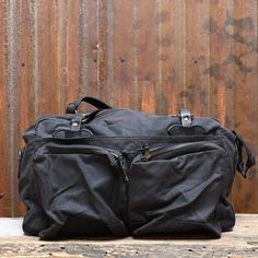 View of front of duffle Black Coated Canvas Duffle Bag For Travel, Black Duffle Bag With Luggage Sleeve In Coated Canvas, Black Coated Canvas Duffle Bag With Luggage Sleeve, Black Canvas Travel Bag For Overnight Trips, Black Canvas Duffle Bag For Overnight Trips, Black Waxed Canvas Duffle Bag For Travel, Black Waxed Canvas Travel Duffle Bag, Black Waxed Canvas Travel Bag With Leather Handles, Classic Outdoor Bag With Zipper Pocket