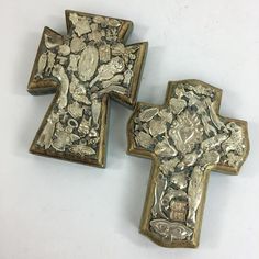 two metal crosses sitting next to each other on a white surface with an image of jesus and the cross