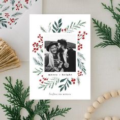 a holiday card with an image of two people kissing in front of evergreen leaves and berries