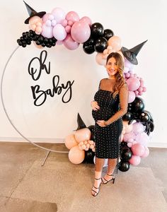 a pregnant woman standing in front of a balloon arch