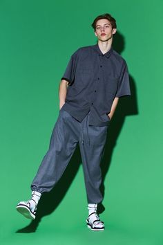 a man standing in front of a green background wearing an oversize shirt and pants