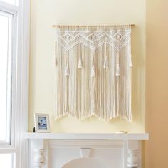 a wall hanging with tassels on top of a mantle in front of a window