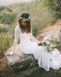 a woman sitting on top of a rock wearing a white dress and holding a bouquet