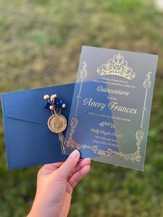 a person holding up a blue and gold wedding card with a brooch on it