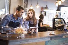 two people sitting at a counter in a restaurant looking at something on a tablet computer