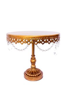 an ornately decorated gold cake stand with crystal beads on the top and bottom, against a white background