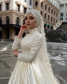 a woman wearing a wedding dress and veil in the middle of a street with buildings behind her