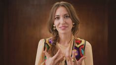 a woman with her hands in the air while wearing a colorful sweater and gold earrings