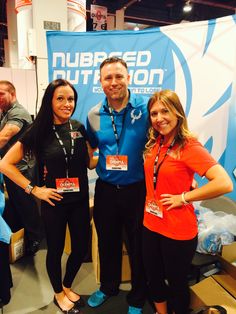 three people posing for a photo in front of a blue and white sign that says numbered nutrition