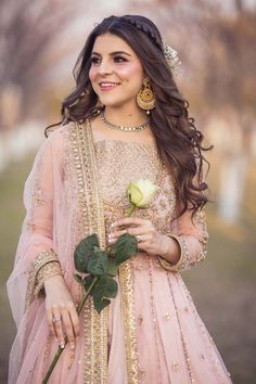 a woman in a pink lehenga holding a rose and smiling at the camera