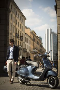 a man standing next to a scooter on a city street with buildings in the background