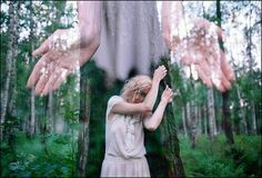 two hands reaching out to touch a woman's face in the woods with her arms outstretched