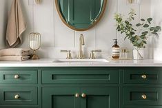 a bathroom with green cabinetry and gold handles on the sink, along with a round mirror