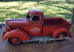 an old red toy truck sitting on top of a wooden table next to a tree