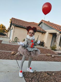 a creepy clown is standing on the sidewalk in front of a house with a red balloon