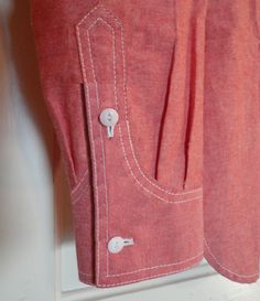 a pair of red pants hanging up on a clothes hanger with two buttons in the pocket