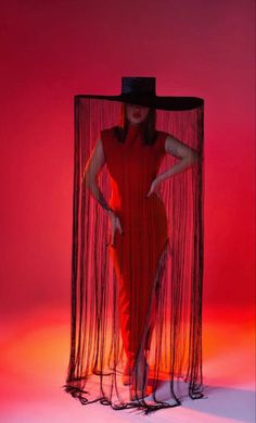 a woman in a red dress and black hat standing next to a large piece of string