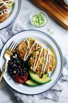 two white plates with food on them sitting on a table next to utensils