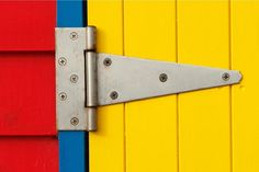 a metal door hinge on the side of a colorful building with red, yellow and blue siding